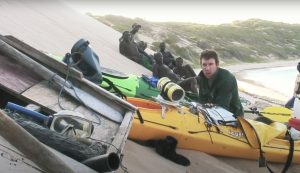 black men on the beach with one white man and various boats